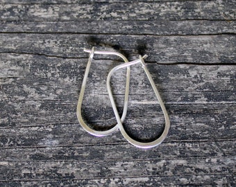 May include: A pair of silver hoop earrings with a teardrop shape. The earrings are on a wooden surface.
