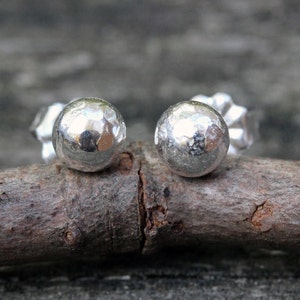May include: A pair of silver stud earrings with a hammered texture. The earrings are round and have a shiny finish.