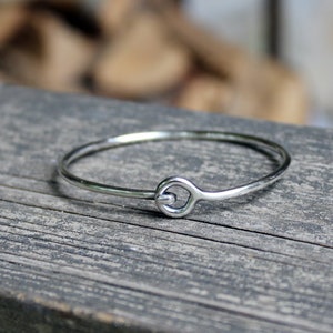 May include: A simple silver bangle bracelet with a unique, twisted, circular clasp.