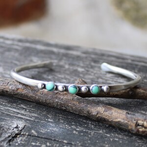 May include: A silver bangle bracelet with a row of five turquoise stones set in silver.