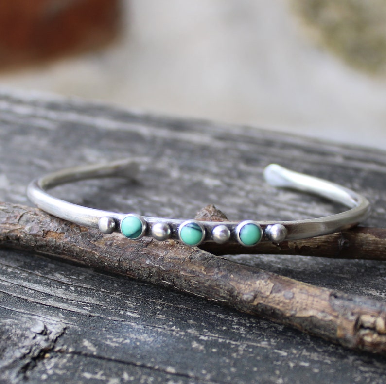 May include: A silver bangle bracelet with a row of five turquoise stones set in silver.