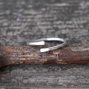 May include: A simple silver ring with a slightly curved design. The ring is open on one side and has a smooth, polished finish.