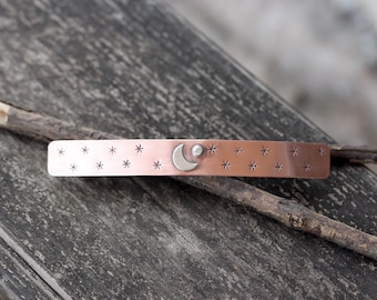 May include: A copper hair clip featuring a crescent moon and a star design. The clip is decorated with small stars.