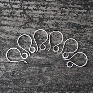 May include: A set of six silver earring hooks, arranged in a semi-circle on a wooden surface.