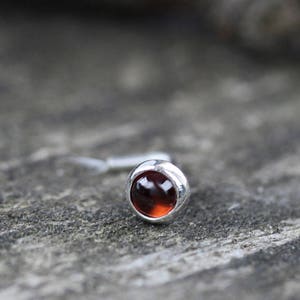 May include: A silver nose ring with a small, round, dark red gemstone.