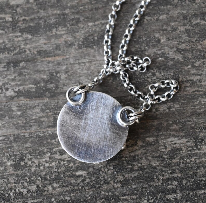 May include: A silver necklace with a round pendant. The pendant has a smooth, brushed finish and is attached to the chain with two small loops.