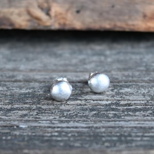 May include: A pair of silver stud earrings with a round, slightly textured design.