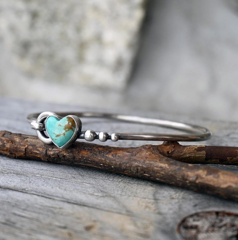 Pode incluir: Uma pulseira de prata com uma pedra turquesa em forma de cora&ccedil;&atilde;o. A pulseira tem um design simples com pequenas contas de prata. A pedra em forma de cora&ccedil;&atilde;o tem tons castanhos e azuis.