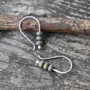 May include: A pair of silver hoop earrings with three green and brown stone beads on each earring.