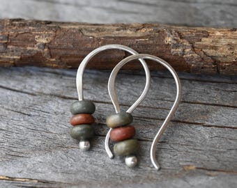 May include: A pair of silver hook earrings featuring three small, rounded beads each. The beads are arranged in a sequence of two muted green beads flanking a single reddish-brown bead in the centre, finished with a small silver ball at the end.
