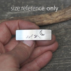 May include: A silver metal bar with a hand-drawn design of mountains and a crescent moon. "Size reference only" is written above the bar.