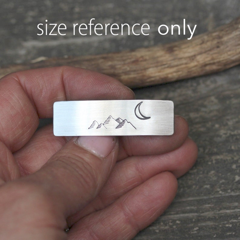 May include: A silver metal bar with a hand-drawn design of mountains and a crescent moon. "Size reference only" is written above the bar.