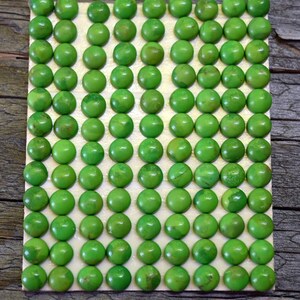 May include: A rectangular grid of ninety small, round, bright green cabochons arranged in ten rows and nine columns. Each cabochon has a smooth, polished, domed surface with subtle variations in color intensity and texture across the set.