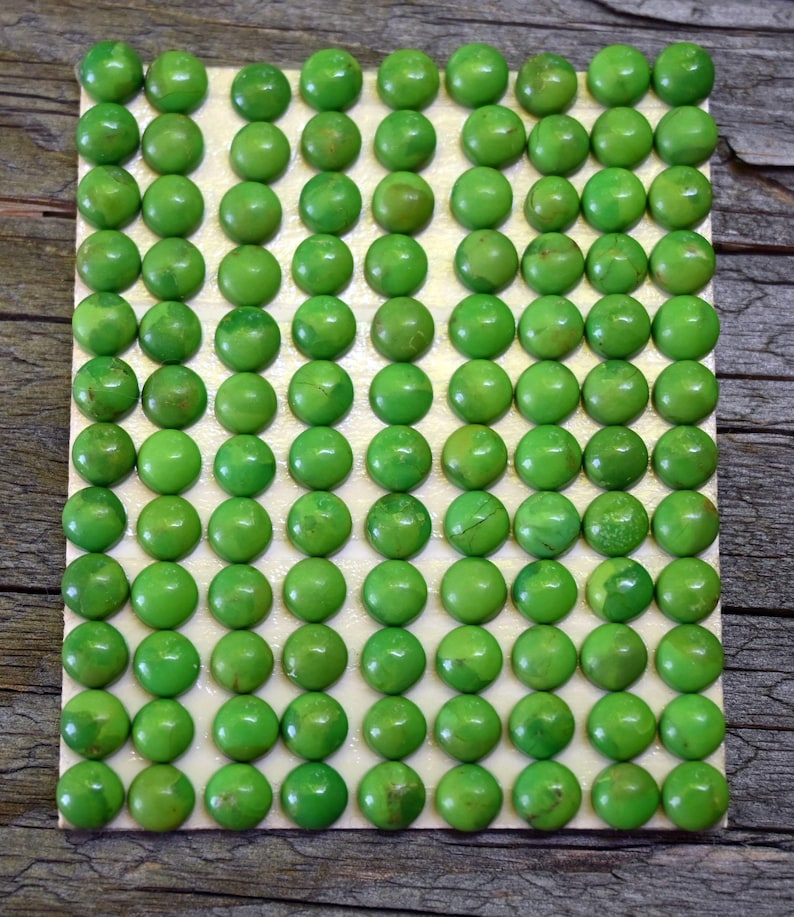 May include: A rectangular grid of ninety small, round, bright green cabochons arranged in ten rows and nine columns. Each cabochon has a smooth, polished, domed surface with subtle variations in color intensity and texture across the set.