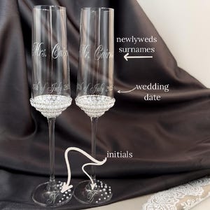 Puede incluir: Dos copas de champán transparentes con borde de cuentas y grabadas con el texto "Mrs. Cain 5th of July 2012" y "Mr. Cain 5th of July 2012". Las copas están sobre una superficie negra con una superposición de encaje blanco.