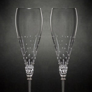 May include: Two clear glass champagne flutes with black stems and crystal embellishments. The flutes are on a black background.