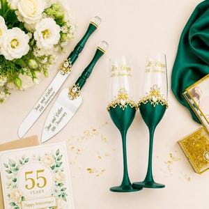 May include: A cake knife and server set with emerald green handles, gold accents, and clear crystal toppers, alongside two matching emerald green champagne flutes engraved with "Mrs. Chague 50th Anniversary" and gold filigree embellishments.