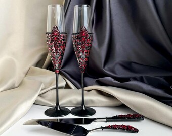 May include: Two black champagne flutes with red and black decorative designs and a black cake server with a red handle.