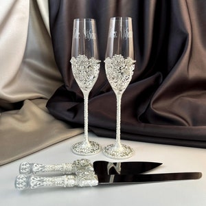 Könnte beinhalten: Zwei silberne Champagnerflöten mit einem dekorativen Design und den eingravierten Worten "Mr. Shaw" und "Mrs. Shaw". Ein silbernes Kuchenschaber mit einem dekorativen Griff ist ebenfalls enthalten.