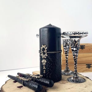 May include: Black pillar candles with gold and black embellishments, and two black and silver etched glass candle holders.