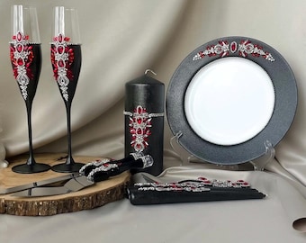 May include: Black wedding cake serving set with red and silver embellishments. The set includes two champagne flutes, a cake knife, a cake server, and a candle.