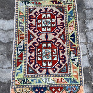 Puede incluir: Una alfombra turca tradicional con un patrón geométrico en tonos rojos, azules, verdes y beige. La alfombra tiene un borde de flecos y está hecha de lana.