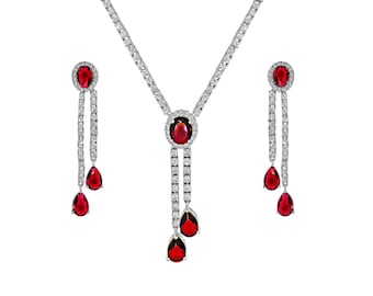May include: A silver necklace and earrings set with red gemstone accents. The necklace features a teardrop-shaped pendant with a larger oval-shaped gemstone in the center. The earrings are also teardrop-shaped with a smaller oval-shaped gemstone in the center.