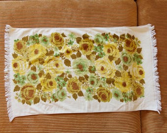 May include: White cotton tea towel with a floral pattern of yellow, brown, and green roses. The towel has a fringed edge.