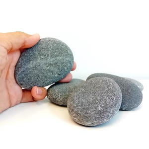 May include: A collection of smooth, gray river rocks. The rocks are oval shaped and have a natural, textured surface.