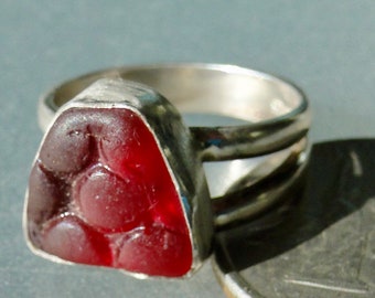 May include: A silver ring with a red, faceted, triangular gemstone. The gemstone has a pattern of circles on its surface.
