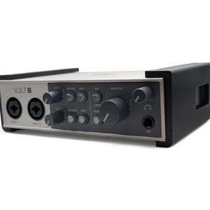 Könnte beinhalten: Ein silbernes und schwarzes Audio-Interface mit dem Text "VOLT 2" auf der Vorderseite. Es verfügt über zwei Eingangsbuchsen, Drehregler für Gain, Monitor und andere Einstellungen sowie eine Kopfhörerbuchse.