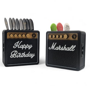 Pu&ograve; includere: Due mini amplificatori per chitarra Marshall neri e dorati. Un amplificatore ha il testo "Happy Birthday" sul davanti. L'altro amplificatore ha il testo "Marshall" sul davanti.