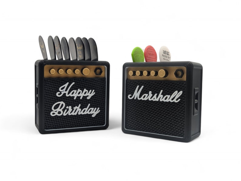 Pu&ograve; includere: Due mini amplificatori per chitarra Marshall neri e dorati. Un amplificatore ha il testo "Happy Birthday" sul davanti. L'altro amplificatore ha il testo "Marshall" sul davanti.