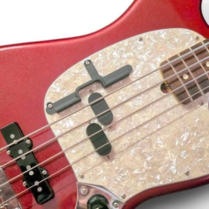 May include: A red electric bass guitar with a white pearloid pickguard and black pickup covers. The guitar has a chrome bridge and tuning pegs.
