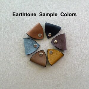 May include: Seven leather cord end tips in various earth tones, including brown, tan, blue, black, and gray. Each tip has a silver metal button.