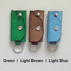 Puede incluir: Tres llaveros de cuero con anillos de metal. Los llaveros son verde, marr&oacute;n claro y azul claro.