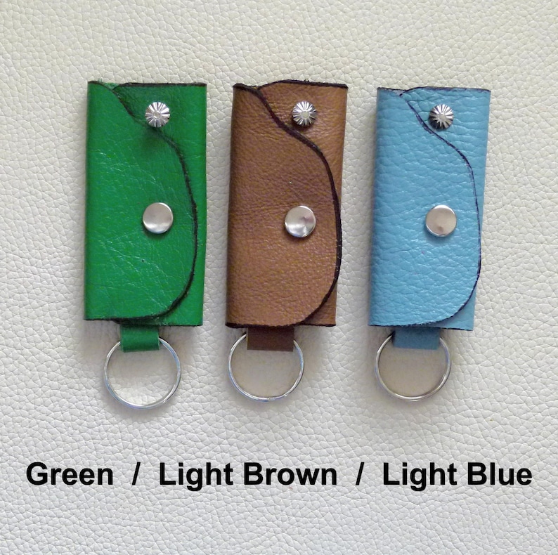 Puede incluir: Tres llaveros de cuero con anillos de metal. Los llaveros son verde, marr&oacute;n claro y azul claro.