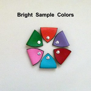 May include: Six leather corner bookmarks in a circle, each with a different color: red, green, purple, pink, blue, and red. Each bookmark has a silver rivet in the center.