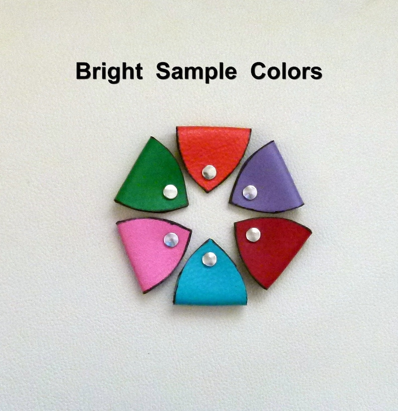 May include: Six leather corner bookmarks in a circle, each with a different color: red, green, purple, pink, blue, and red. Each bookmark has a silver rivet in the center.
