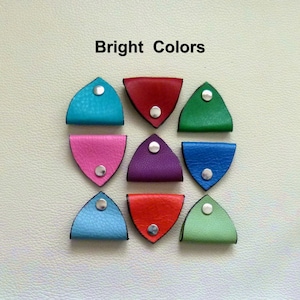 May include: Nine leather cord keepers in various bright colors, including red, blue, green, purple, and pink. Each keeper has a silver metal button.