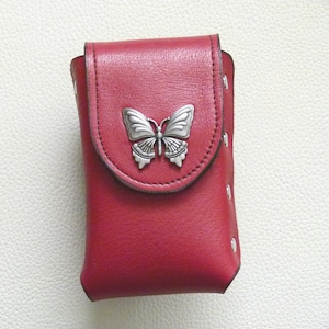 May include: A red leather phone case with a silver butterfly design. The case has a flap that closes with a snap.
