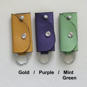 Puede incluir: Tres llaveros de cuero con anillos met&aacute;licos y cierres a presi&oacute;n. Los llaveros son de color dorado, morado y verde menta.