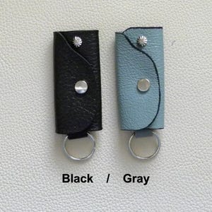 Puede incluir: Dos llaveros de cuero, uno negro y otro gris, con anillos y broches de metal plateado. Los llaveros est&aacute;n etiquetados como "Negro / Gris".
