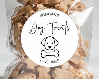 May include: A clear cellophane bag filled with assorted dog treats, tied with a brown ribbon. A white circular label reads "Homemade Dog Treats" with a dog and bone graphic, and "Love, Kristi". The treats are various shapes and sizes.