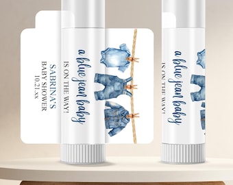 May include: Two lip balm tubes and a card with the text "a blue jean baby IS ON THE WAY!" and "SABRINA'S BABY SHOWER 10.21.xx". The tubes and card feature a watercolor design of denim clothing hanging on a clothesline.