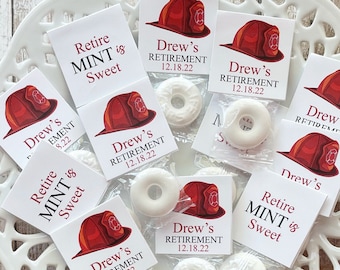 May include: A white, decorative, openwork plate holds individually wrapped mint candies and small cards. The cards feature a red firefighter's helmet graphic and text that reads "Drew's Retirement 12.18.22" and "Retire MINT is Sweet."