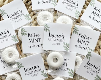 May include: Small clear bags containing white mint candies, each paired with a white card. The cards feature the text "Laura's Retirement 3.17.23" and "Retire-MINT is Sweet!" with green leaf accents, arranged on a woven surface.