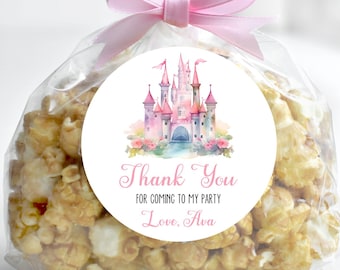 May include: A clear cellophane bag filled with popcorn, tied with a pink ribbon. A round label with a pink castle design and the text "Thank You for coming to my party, Love, Ava" is affixed to the bag. The text "Printed Labels" is in a black circle.