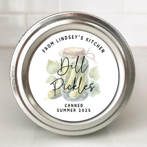May include: A metal lid with a label that reads "From Lindsey's Kitchen" and "Dill Pickles Canned Summer 2025". The label features a watercolor illustration of a jar of pickles with green leaves.