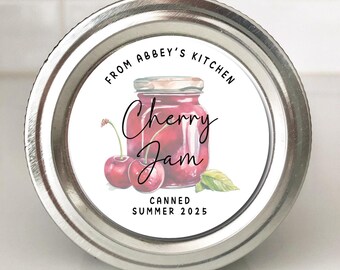 May include: A small, round jar with a silver lid. The label reads "From Abbey's Kitchen" and features a watercolor illustration of cherry jam, cherries, and a leaf. The text "Cherry Jam" is written in cursive, with "Canned Summer 2025" below.